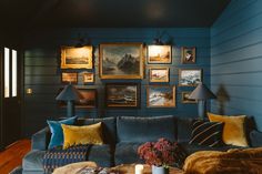 a living room with blue walls and pictures on the wall above the couch, along with a coffee table