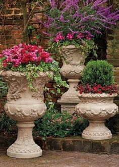 three large vases with flowers in them sitting on the side of a brick wall