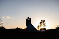 a bride and groom are silhouetted against the setting sun