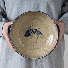 a person holding a bowl with a fish painted on the side in it's center