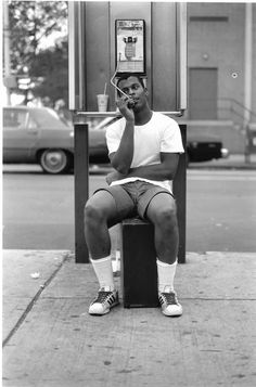 a man sitting on top of a box talking on a cell phone next to a parking meter