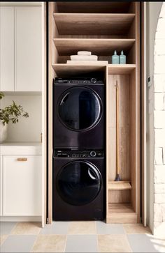 a black washer and dryer in a wooden cabinet next to white cupboards