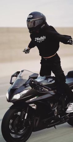 a man riding on the back of a black motorcycle down a road with his arms outstretched