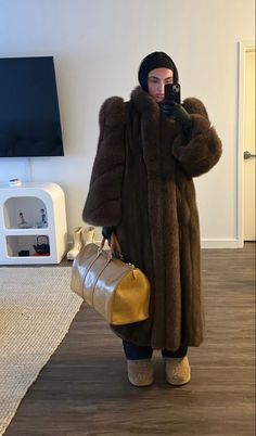 a woman in a fur coat taking a selfie with her cell phone while holding a handbag