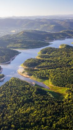 an aerial view of a river surrounded by green trees and mountains in the distance, with sunlight shining on the water