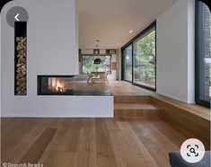 a living room with wood floors and a fire place in the center, surrounded by large windows