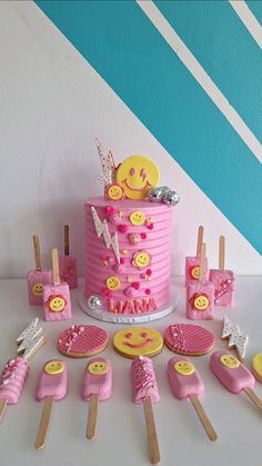 a pink cake surrounded by cupcakes and candy sticks with smiley faces on them