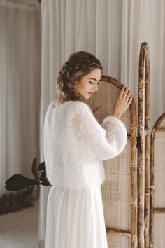 a woman in a white dress standing next to a bamboo chair and looking at the wall