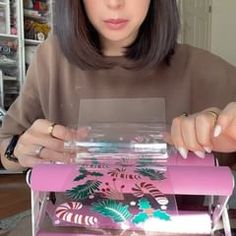 a woman is looking at the inside of a pink box with flowers and leaves on it