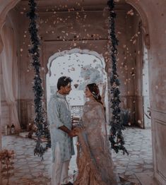 a man and woman standing in front of an archway with flowers on the ground around them