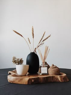 a black vase sitting on top of a wooden table next to two white bowls filled with plants