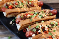 three hot dogs with toppings on a black plate