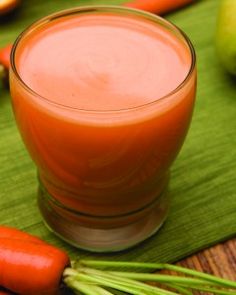 carrot juice in a glass surrounded by fresh fruits and vegetables on a green mat,