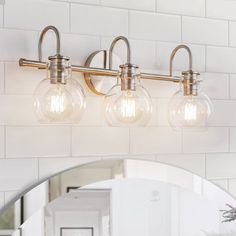 three light bathroom fixture with clear glass globes and brass finish on white tile wall