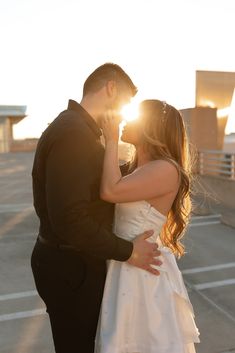 a bride and groom kissing in an empty parking lot with the sun shining through their eyes