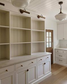 an empty kitchen with white cabinets and wood flooring, along with two lamps hanging from the ceiling