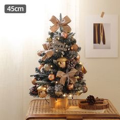 a small christmas tree with gold ornaments and bows on it's top, sitting on a table in front of a window