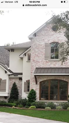 a large brick house with lots of windows and bushes around it's front yard