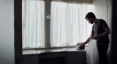 a man standing in front of a window with a plastic bag on his lap and looking at the floor