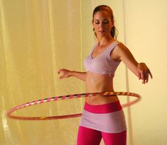 a woman in pink and white outfit holding a hula hoop while standing on top of a wooden floor