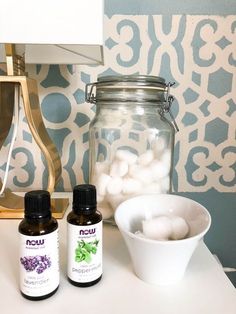 an assortment of essential oils sitting on a table next to a lamp and bowl with cotton balls in it