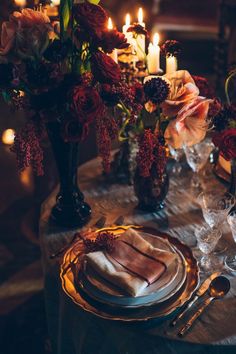 the table is set with candles and flowers in vases, plates and silverware