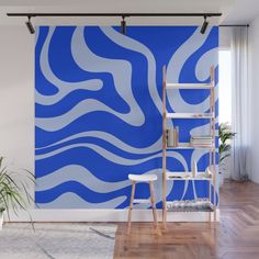 an abstract blue and white wall mural in a living room with wooden floors, a ladder and potted plant