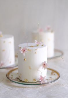 three small white cakes with pink flowers on them and gold trimmings, sitting on a glass plate