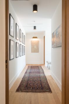 a hallway with pictures on the wall and a rug on the floor in front of it