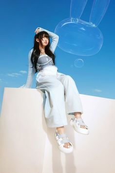 a woman sitting on top of a white wall with bubbles floating in the air behind her