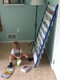 a toddler is sitting on the floor playing with a bookshelf next to a lamp