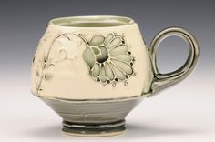 a white and green tea pot with flowers on the inside is sitting in front of a gray background