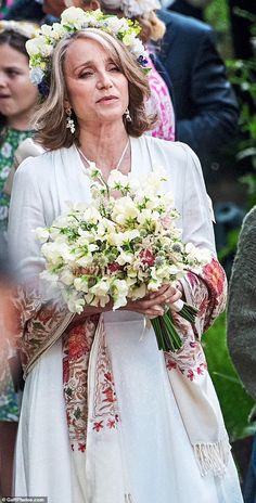 a woman in white dress holding flowers and wearing a wreath on top of her head