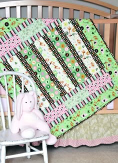 a pink stuffed animal sitting next to a baby quilt on a crib in a bedroom