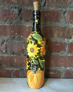 a bottle with sunflowers painted on it is sitting against a brick wall and has a cork top