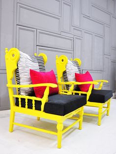 two yellow chairs sitting next to each other in front of a gray wall with red and black pillows