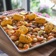 corn on the cob and potatoes in a pan with lemon wedged garnishes