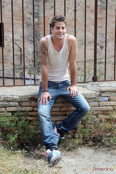 a young man sitting on top of a stone wall next to a fence and gate