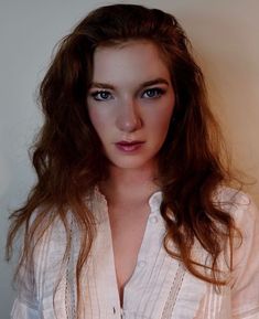 a woman with long brown hair and blue eyes posing for a photo in a white shirt