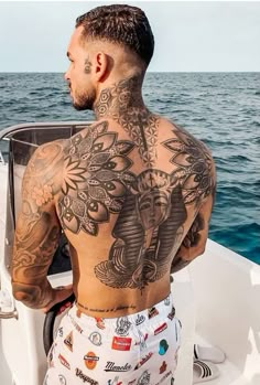 a man with tattoos on his back sitting in a boat looking out at the ocean