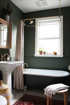 a bath tub sitting next to a sink under a window in a room with green walls