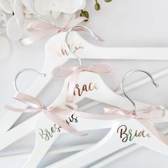 three white hangers with pink ribbons and the names of bride and groom on them