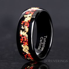 black ceramic ring with gold and red flowers inlaying the center, on a reflective surface