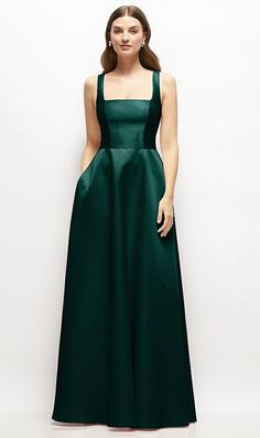 a woman in a long green dress standing against a white wall with her hands on her hips