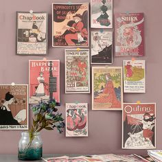 a vase filled with flowers sitting next to a wall covered in old fashioned poster art