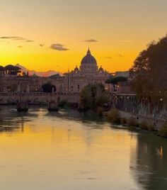 the sun is setting over a river with buildings in the background