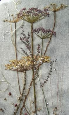 three dried flowers in a vase on a white tablecloth with blue trimmings