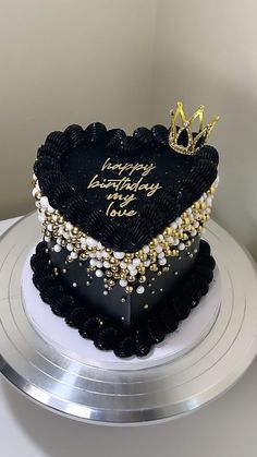 a black and gold heart shaped birthday cake on a silver platter with a crown