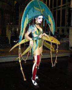 a woman dressed in costume with feathers and chains around her neck, standing on stage