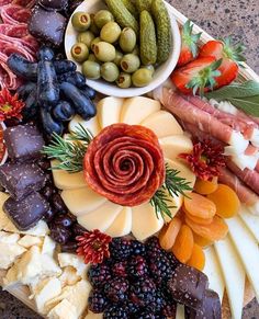 a platter filled with different types of cheeses, meats and fruit on top of each other